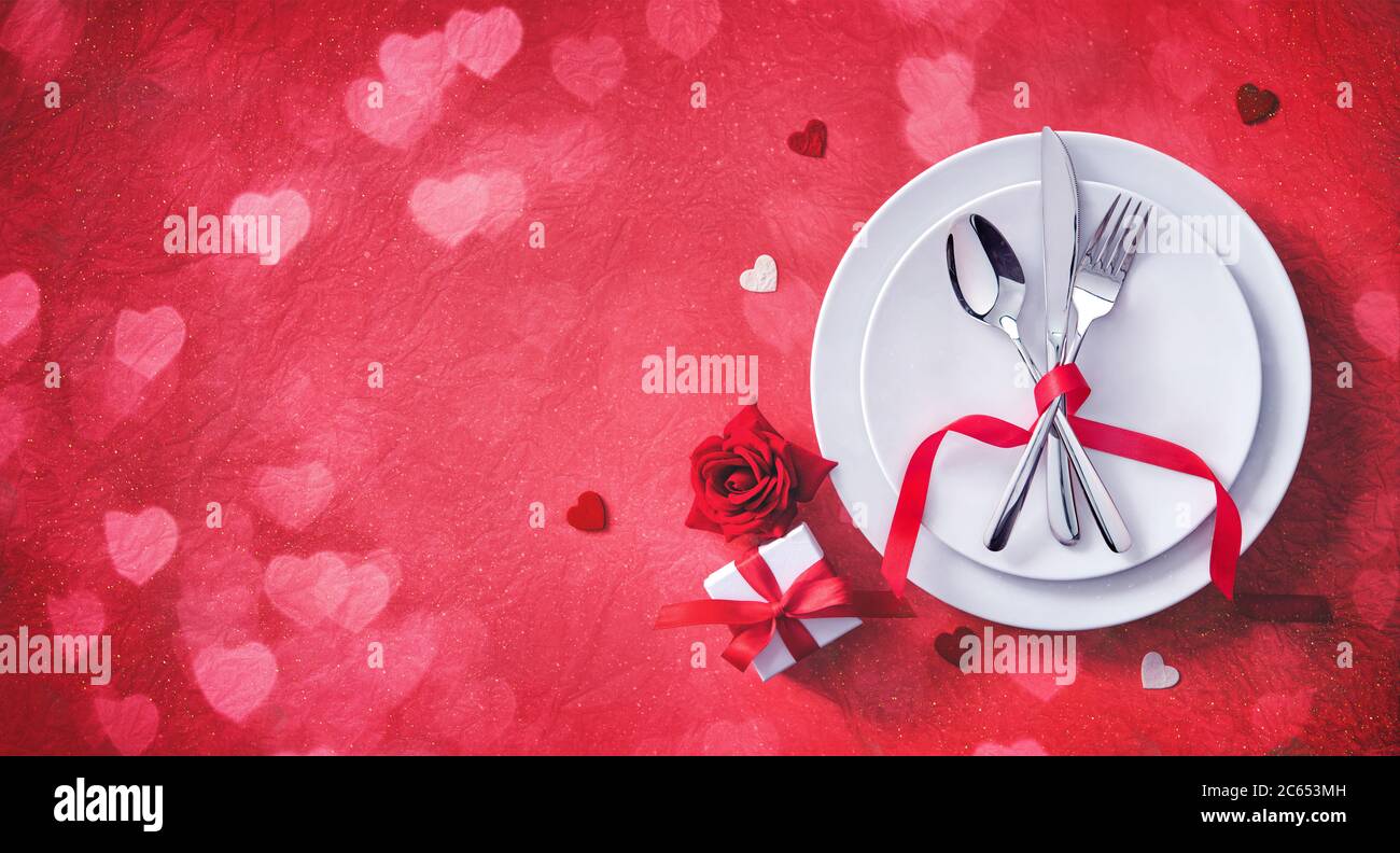 Mesa roja cubiertos con decoración de corazones, caja de regalo y rosa para la cena de los días de San Valentín Foto de stock