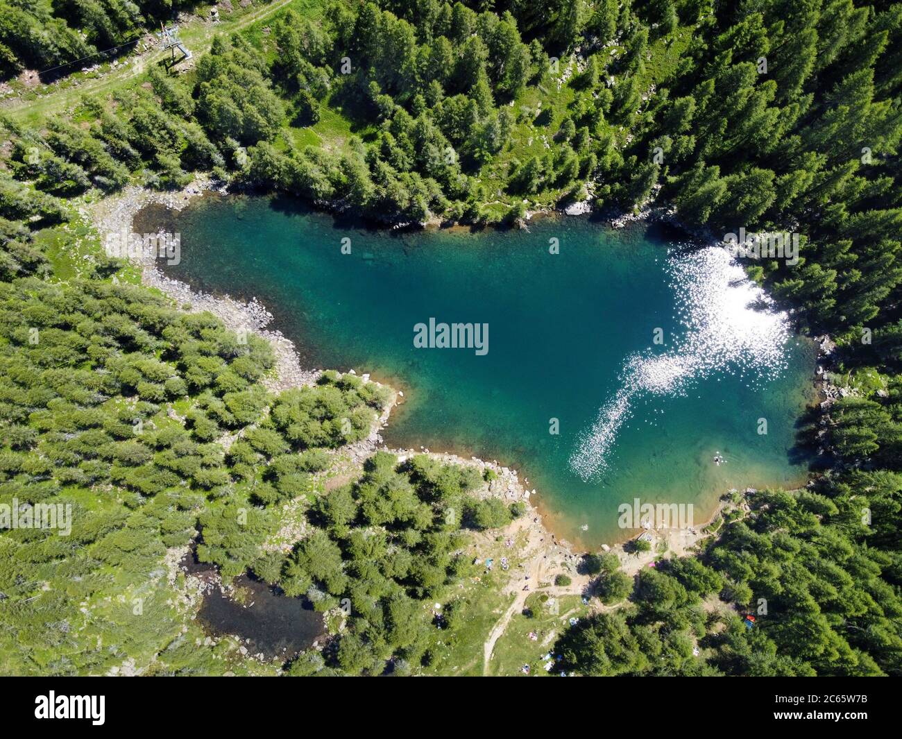 Vista aérea de un lago azul claro de montaña rodeado de bosques de coníferas verdes en un día soleado tirado de un drone Foto de stock