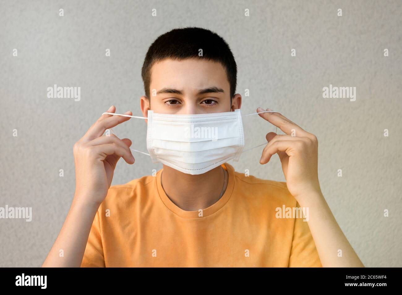 Adolescente sosteniendo una máscara en las manos frente a su cara para el control de la infección durante el coronavirus o la pandemia de Covid-19 contra un blanco Foto de stock