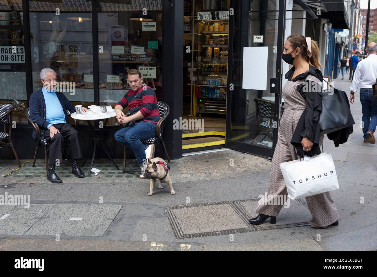 Con las reglas de bloqueo de la pandemia de Coronavirus siendo aliviadas, los pubs y los negocios de restaurantes están reabriendo lentamente y los clientes con distanciamiento social y su perro se sientan fuera de un café y la gente-observa en Wardour Street en Soho, en el West End de la capital, el 6 de julio de 2020, en Londres, Inglaterra. Foto de stock