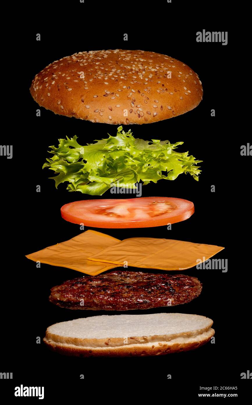 Ingredientes voladores hamburguesas o cheeseburger en una pequeña tabla de  madera aislada sobre un fondo oscuro. Burger flotando en el aire sobre la  mesa. S Fotografía de stock - Alamy