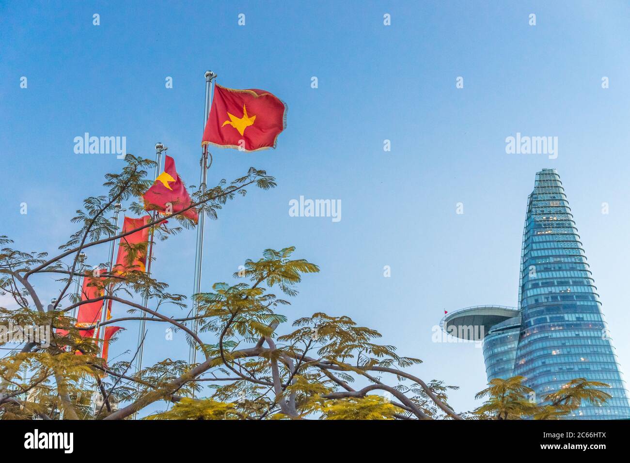 Bitexco torre bajo el cielo azul junto a una fila de banderas vietnamitas y las banderas del Partido Comunista de Vietnam en la ciudad de Ho Chi Minh, Vietnam. Concepto de poli Foto de stock