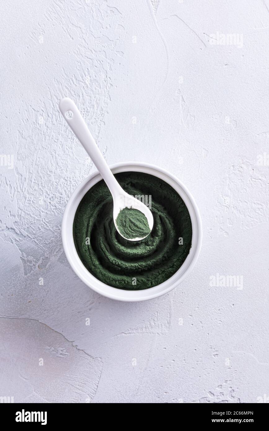 Espiral hecha de clorella verde o polvo de espirulina en un tazón de porcelana blanca desde arriba y cuchara encima de ella. Comida saludable y dieta Foto de stock