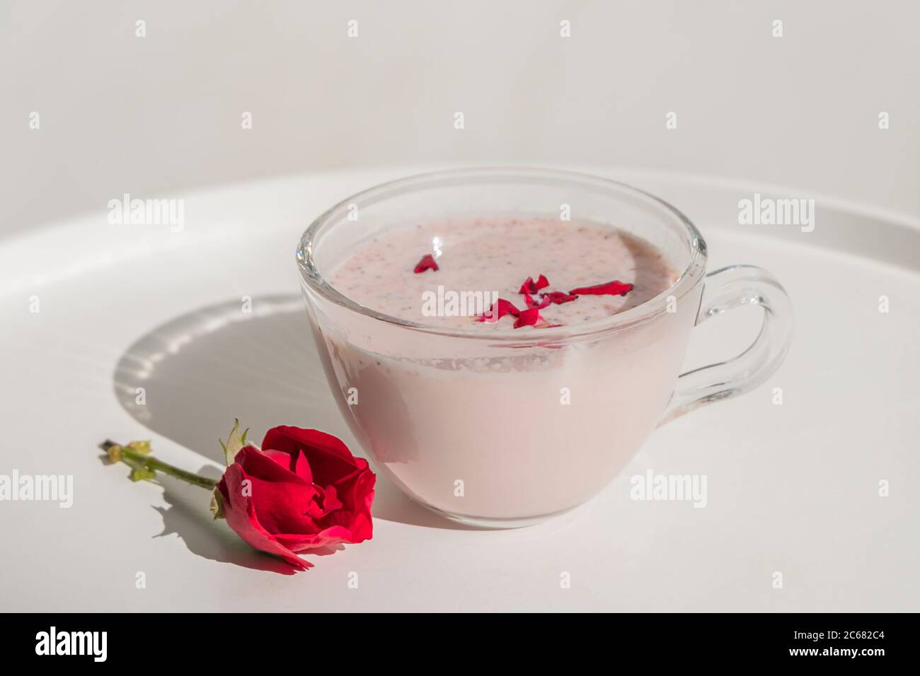 Vaso de vaso de ayurvédico saludable beber leche de luna con rosa en la mesa blanca Foto de stock