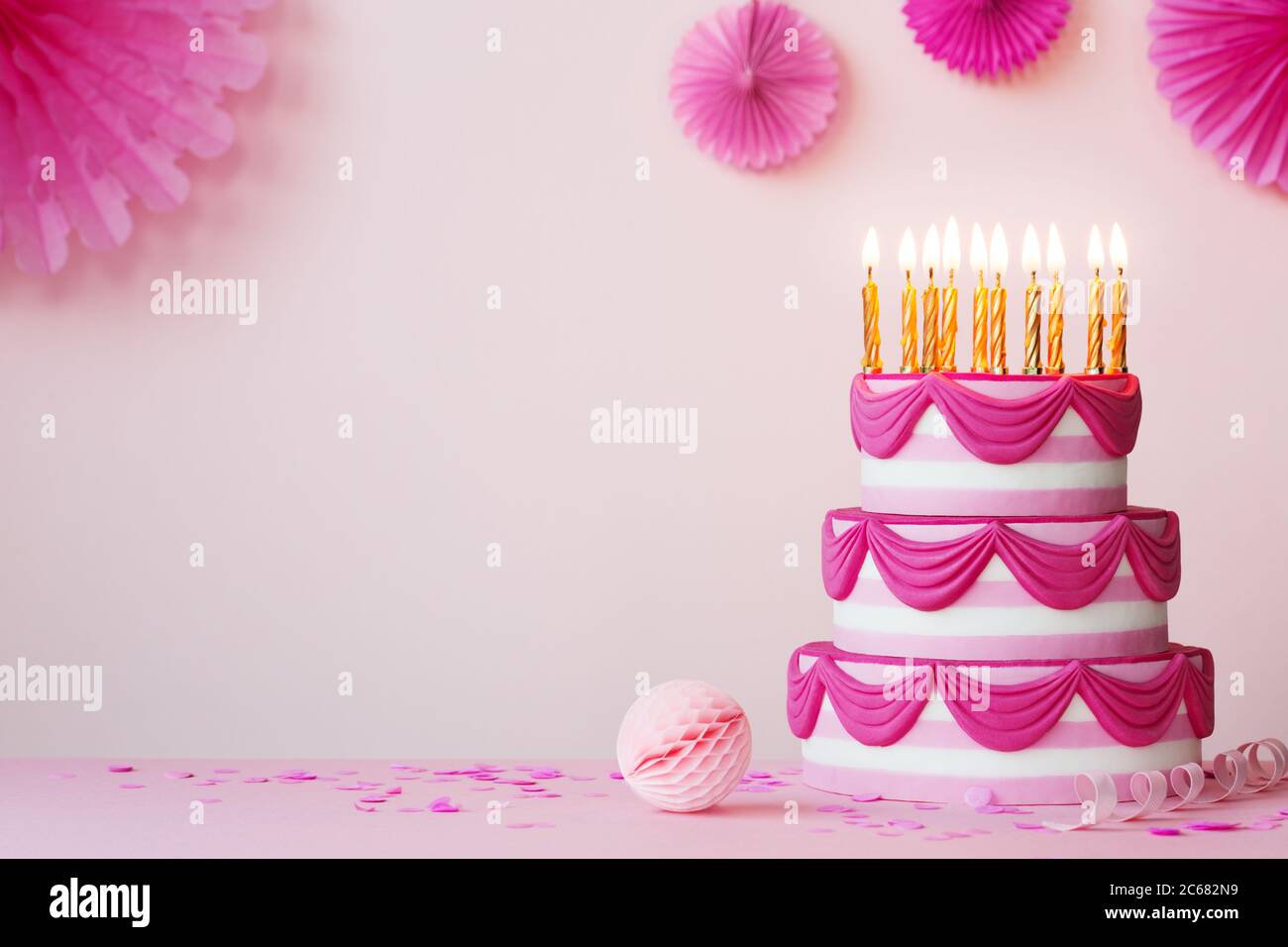Fiesta de cumpleaños con pastel de cumpleaños escalonado rosa y velas doradas Foto de stock