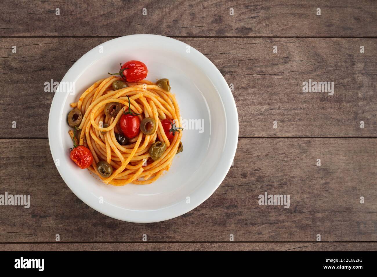 Espaguetis con salsa de tomate y albahaca en un tazón blanco sobre una superficie de madera oscura. Foto de stock