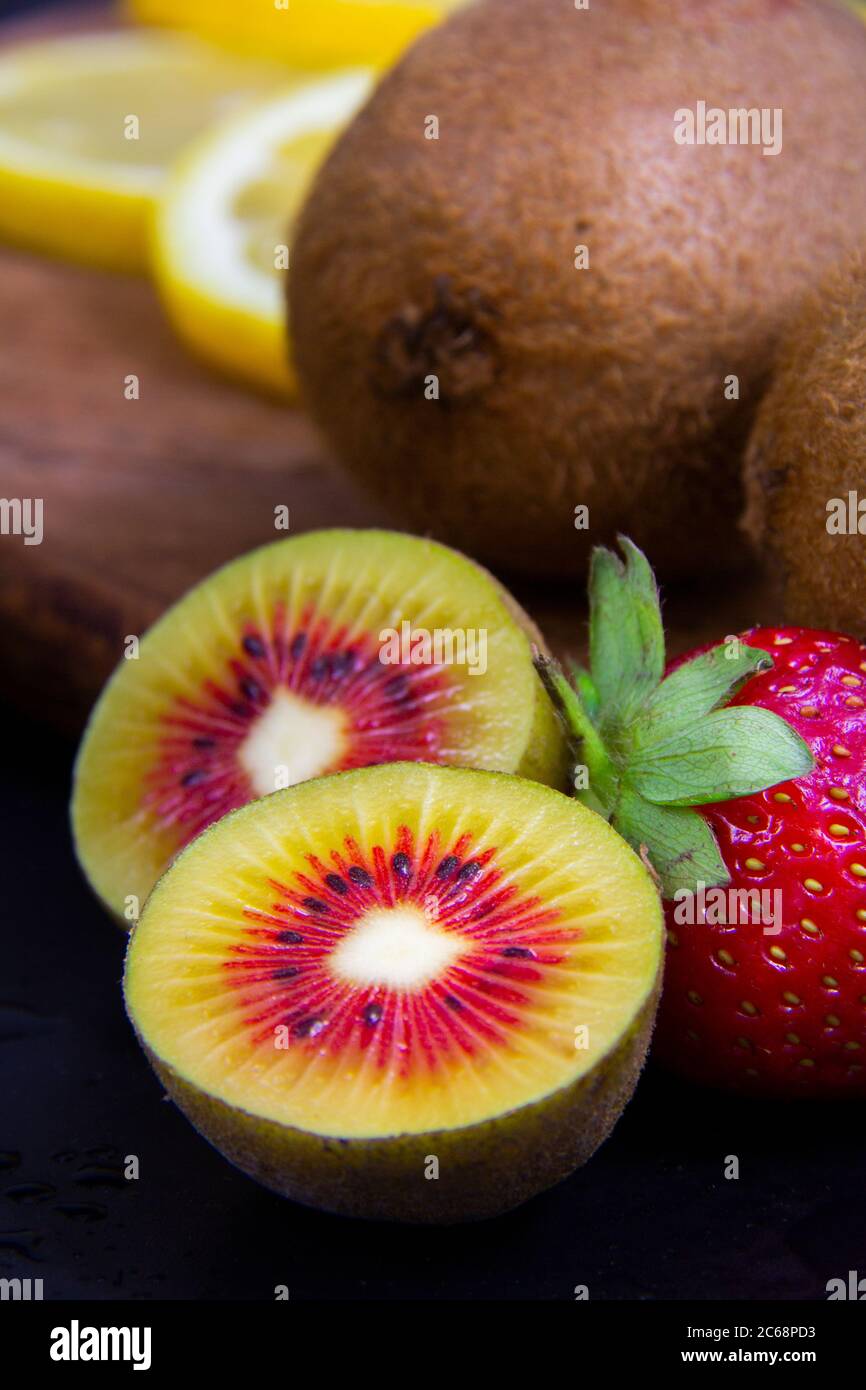 Vista cercana de las frutas diminutas, kiwis verde y rojo, y una fresa roja madura. Foto de stock