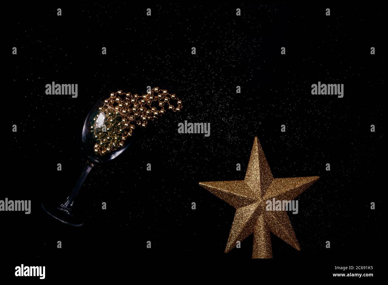Cuentas de oro vertidas de vidrio de vino y estrella sobre fondo negro con espacio de copia para texto. Vista superior. Año nuevo y concepto de Navidad. Foto de stock