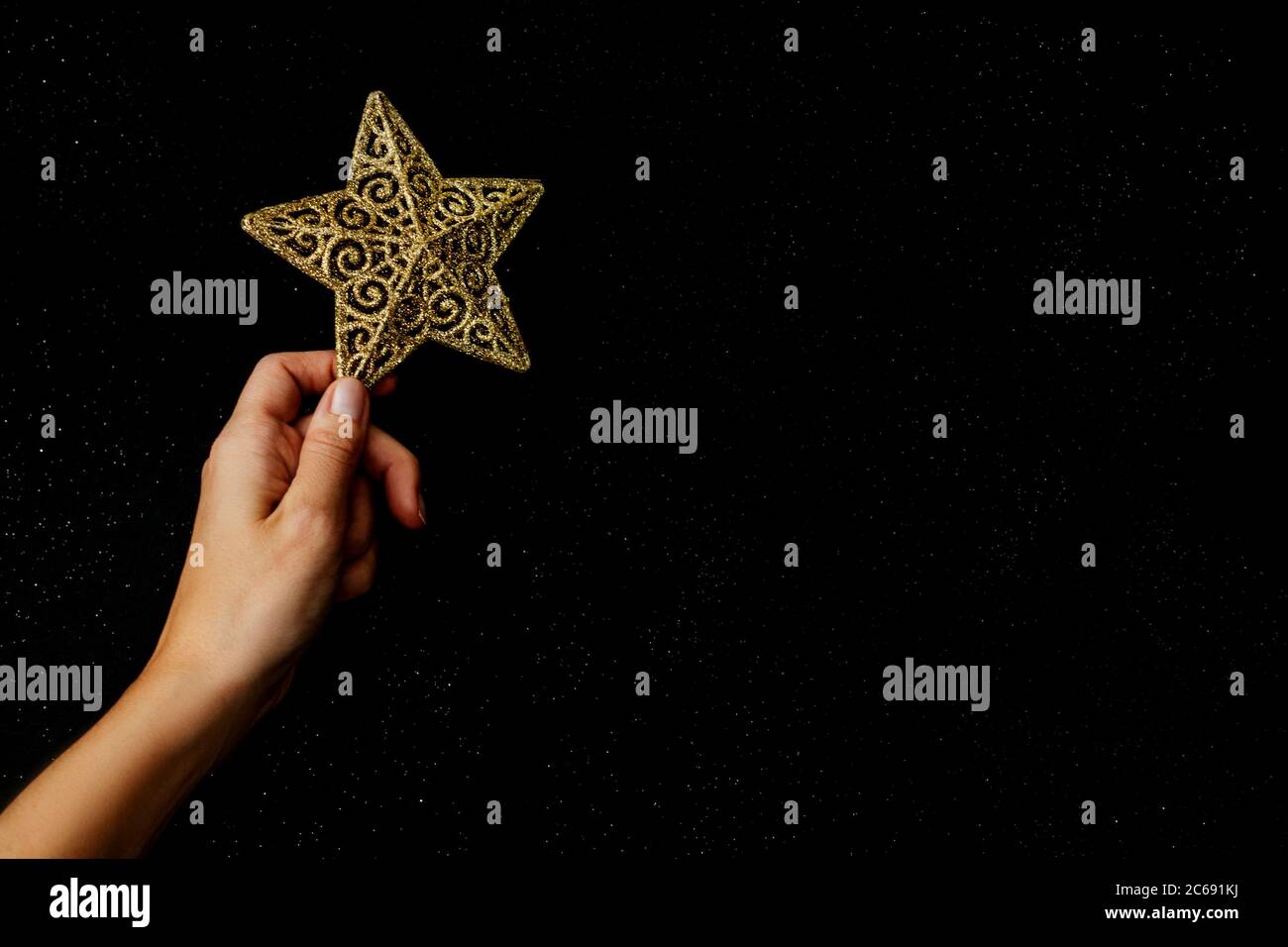 Hermosa composición de Navidad. Estrella dorada en la mano sobre fondo negro como estrellas cielo. Diseño plano. Espacio de copia. Horizontal. Foto de stock