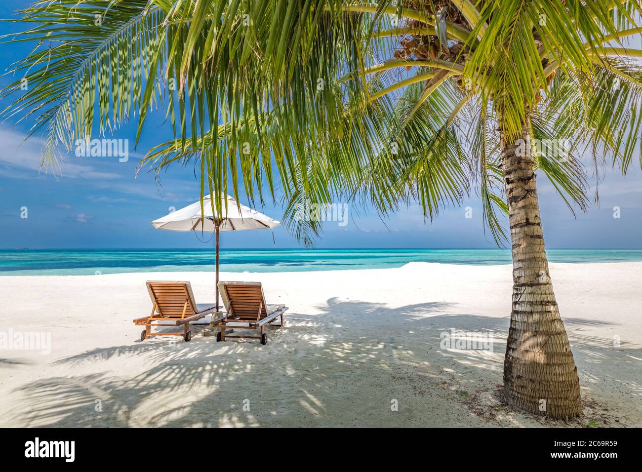Romántico destino de luna de miel en la playa para parejas, sillas de playa con hojas de palma y sombrilla, cerca del mar azul. Unas vacaciones de verano increíbles Foto de stock