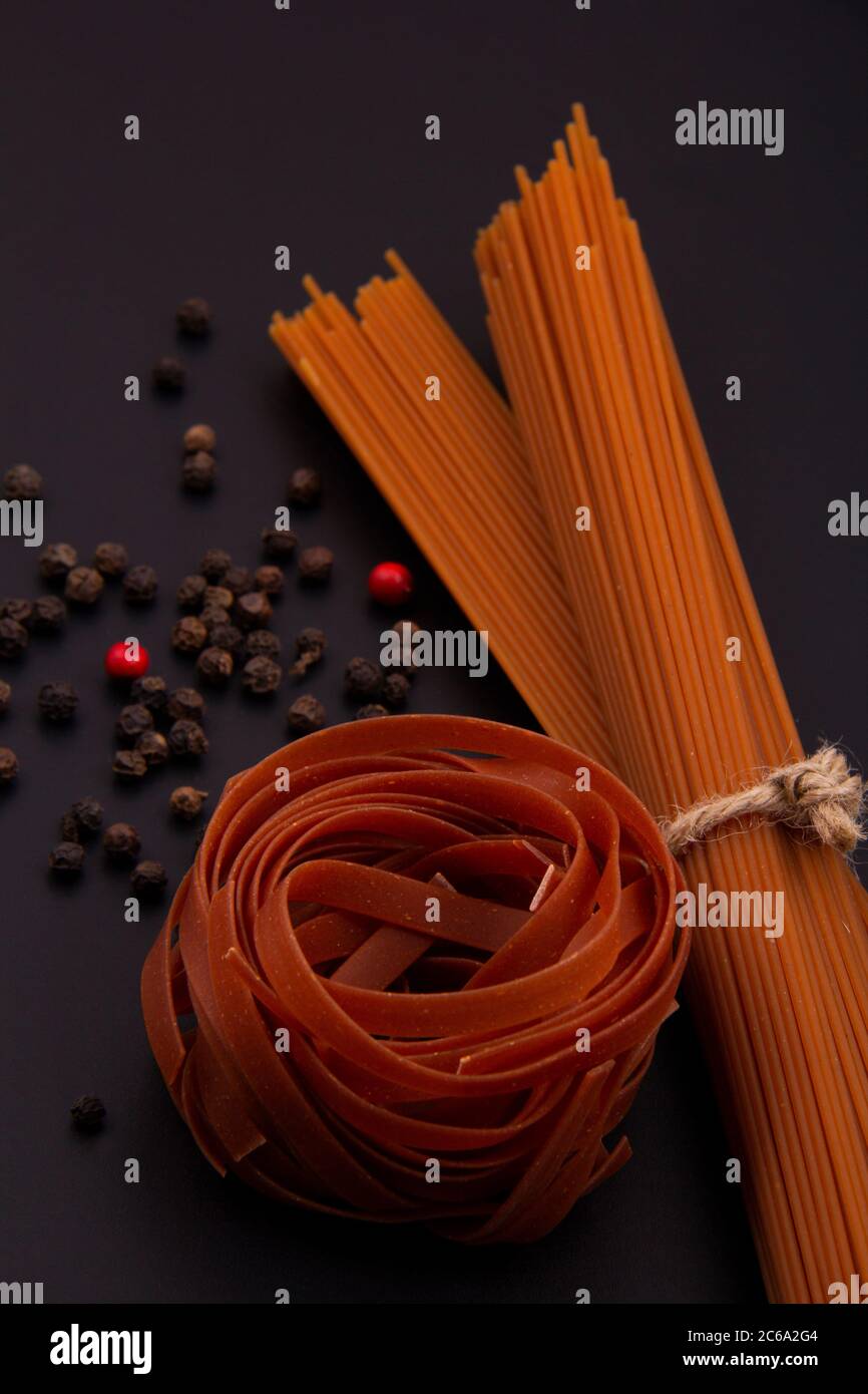 Pasta larga y marrón con diferentes formas y colores con un plato de pimienta. Foto de stock