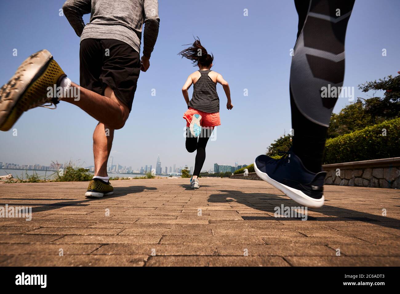 tres jóvenes adultos asiáticos corriendo jogging al aire libre, vista trasera y ángulo bajo Foto de stock
