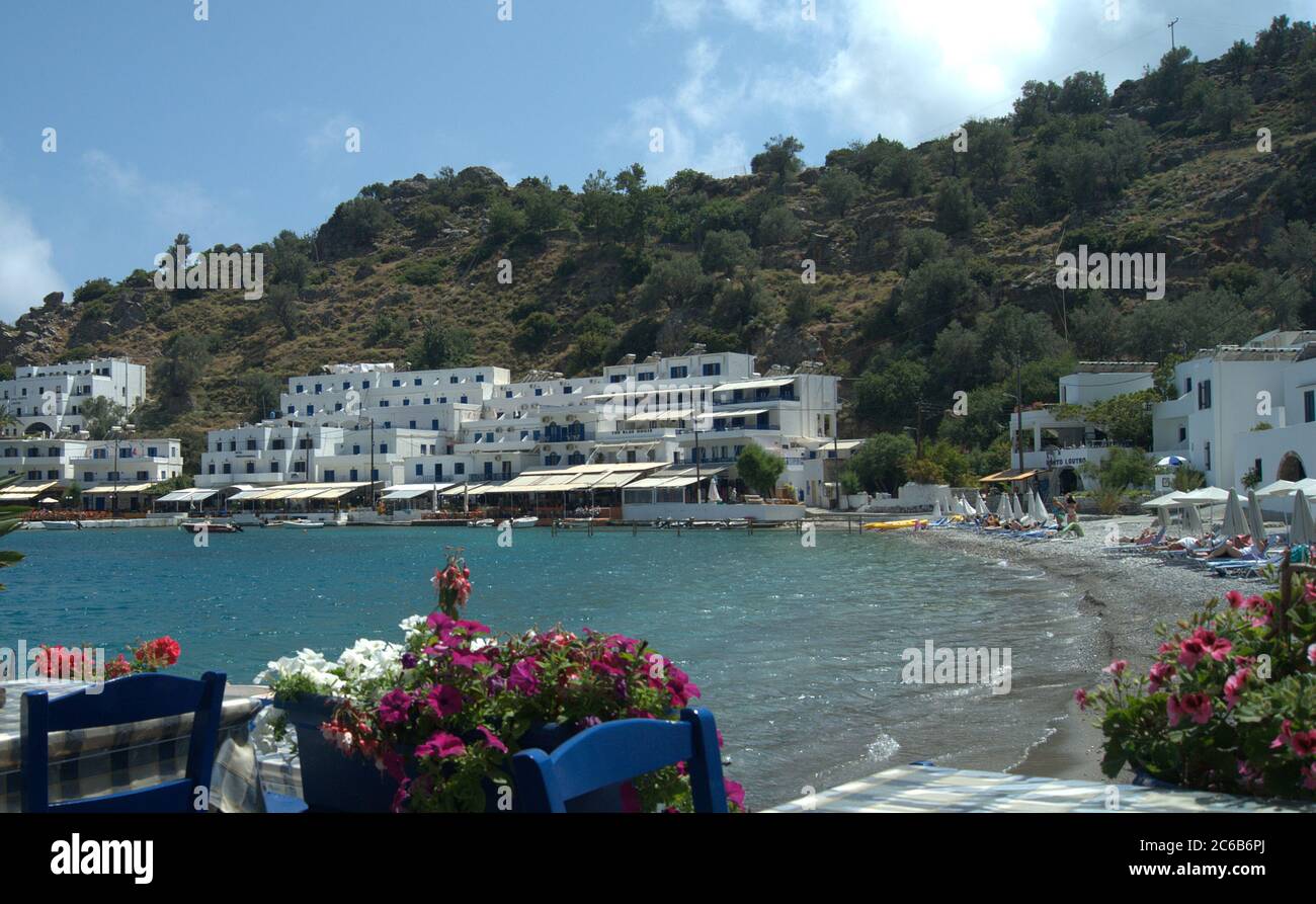 Loutro, Creta, Grecia. Bonita playa con tabernas y bares a lo largo del puerto. Los turistas se relajan bajo el sol. Foto de stock