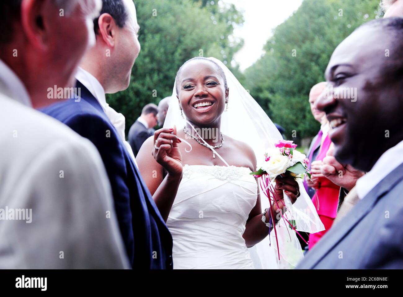 Hermosa, impresionante novia negra de veinte o treinta años sonriendo y  gozosa en su día de la boda y usando un vestido blanco de la boda con velo  y ramo Fotografía de