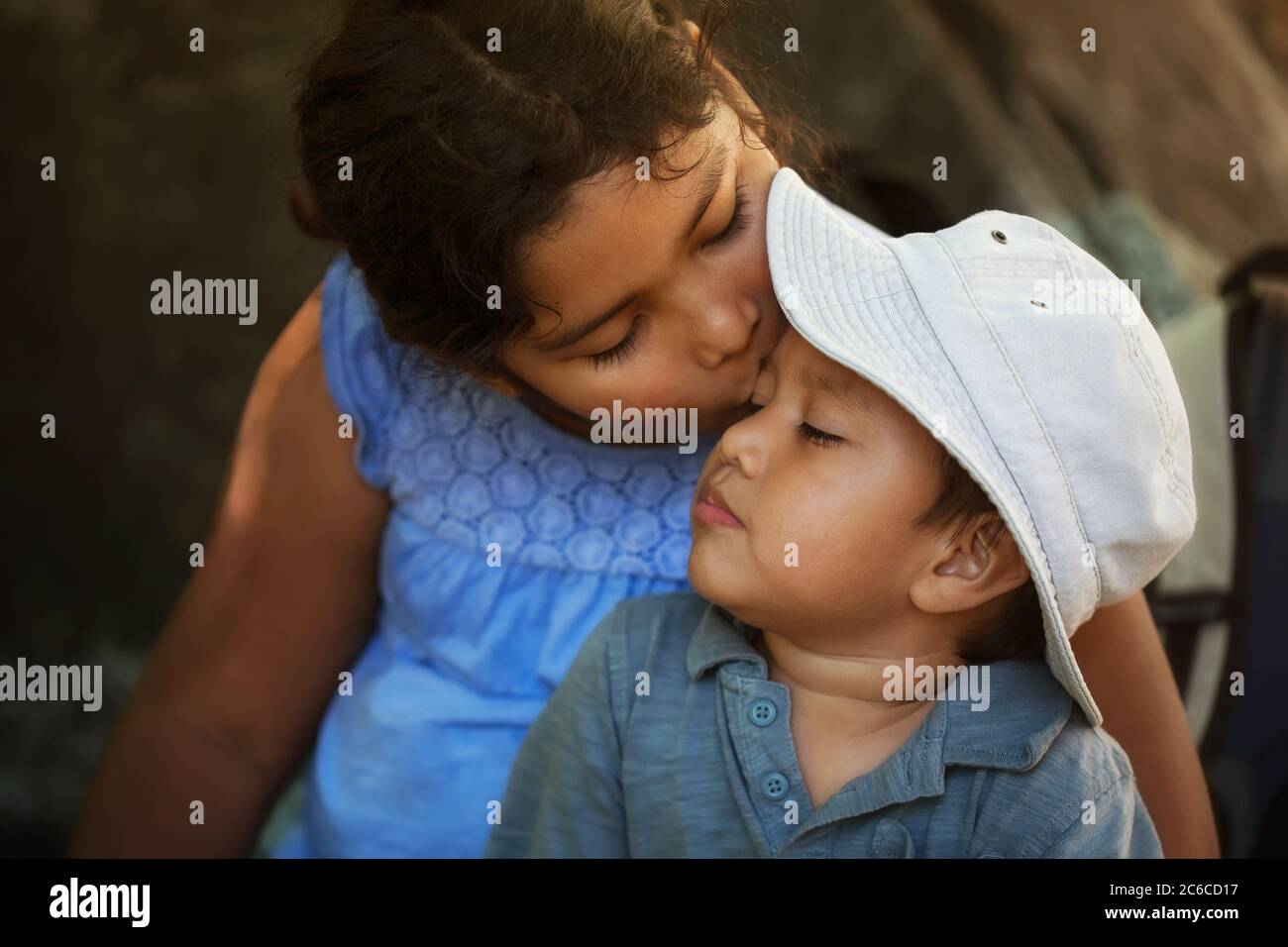 La hermana mayor conforta a su hermano pequeño después de hacerse daño al aire libre, dándole un beso en la frente. Foto de stock