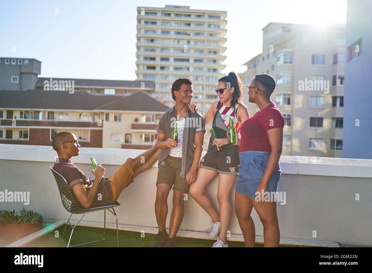 Jóvenes amigos bebiendo cerveza en el soleado balcón urbano de la azotea Foto de stock