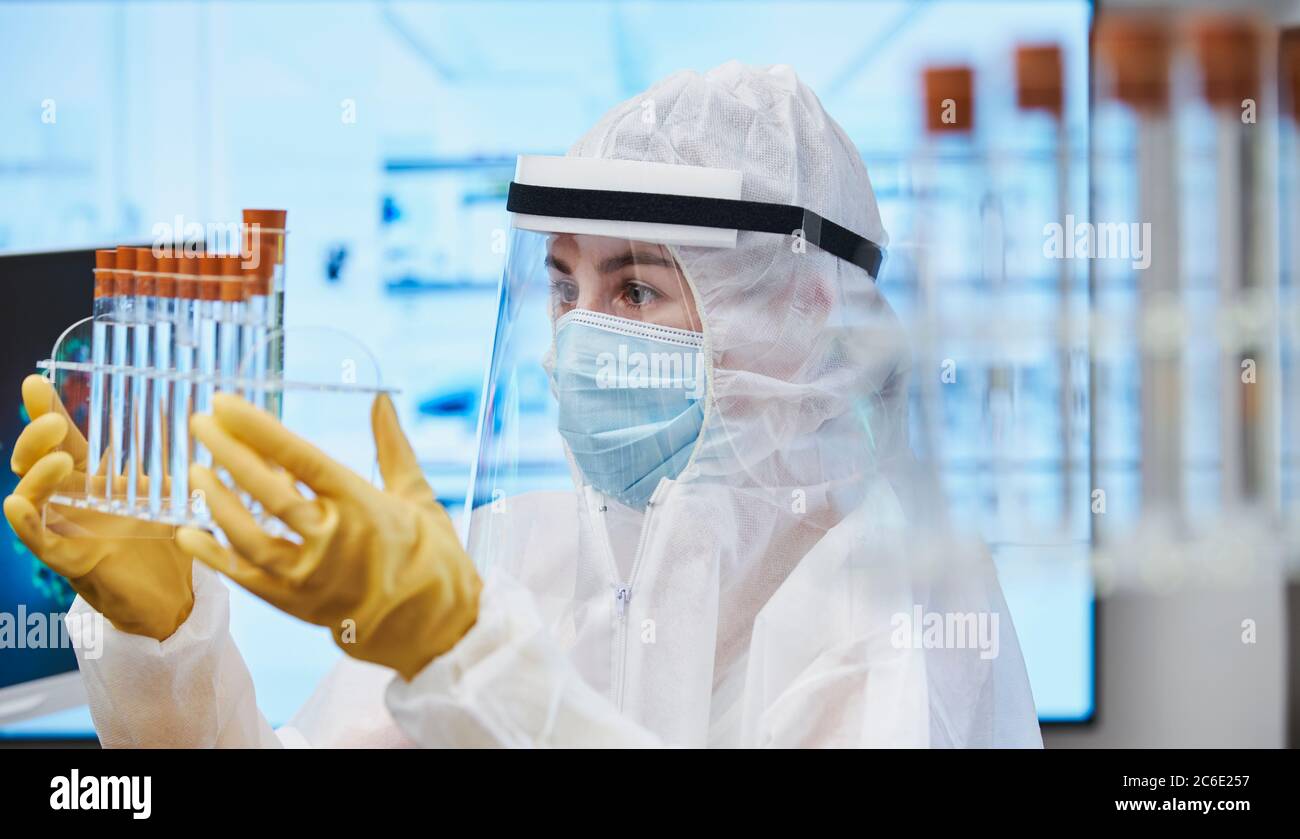 Mujer científica en traje limpio con tubos de ensayo estudiando coronavirus Foto de stock