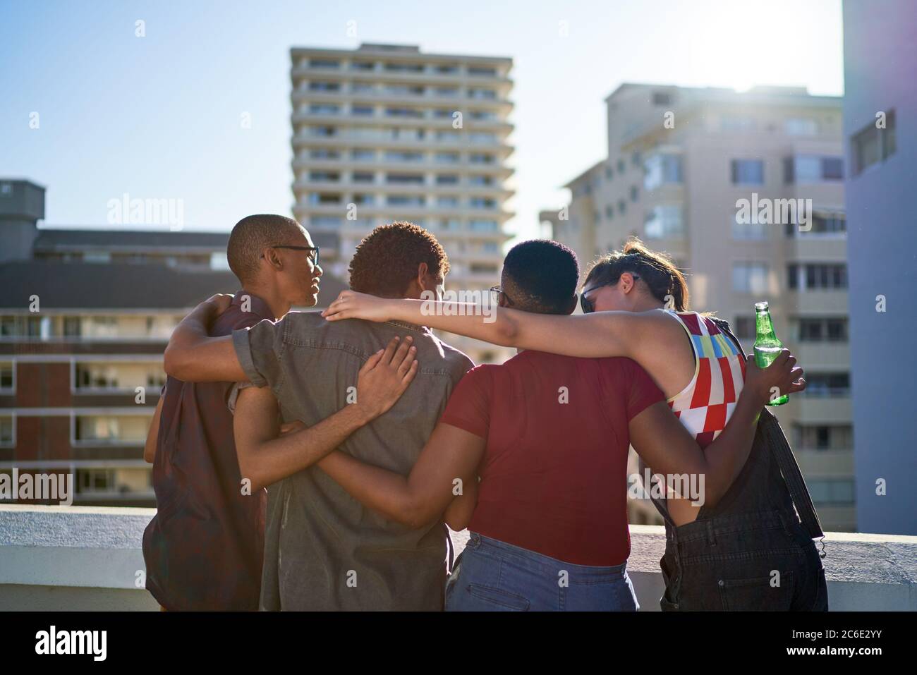Jóvenes amigos abrazando el soleado balcón urbano en la azotea Foto de stock