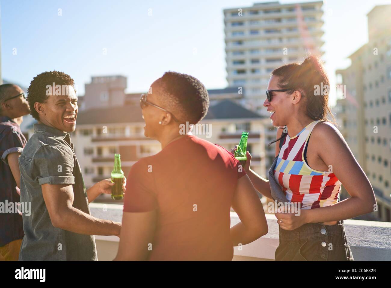Felices amigos jóvenes que cuelgan en el soleado balcón urbano de la azotea Foto de stock