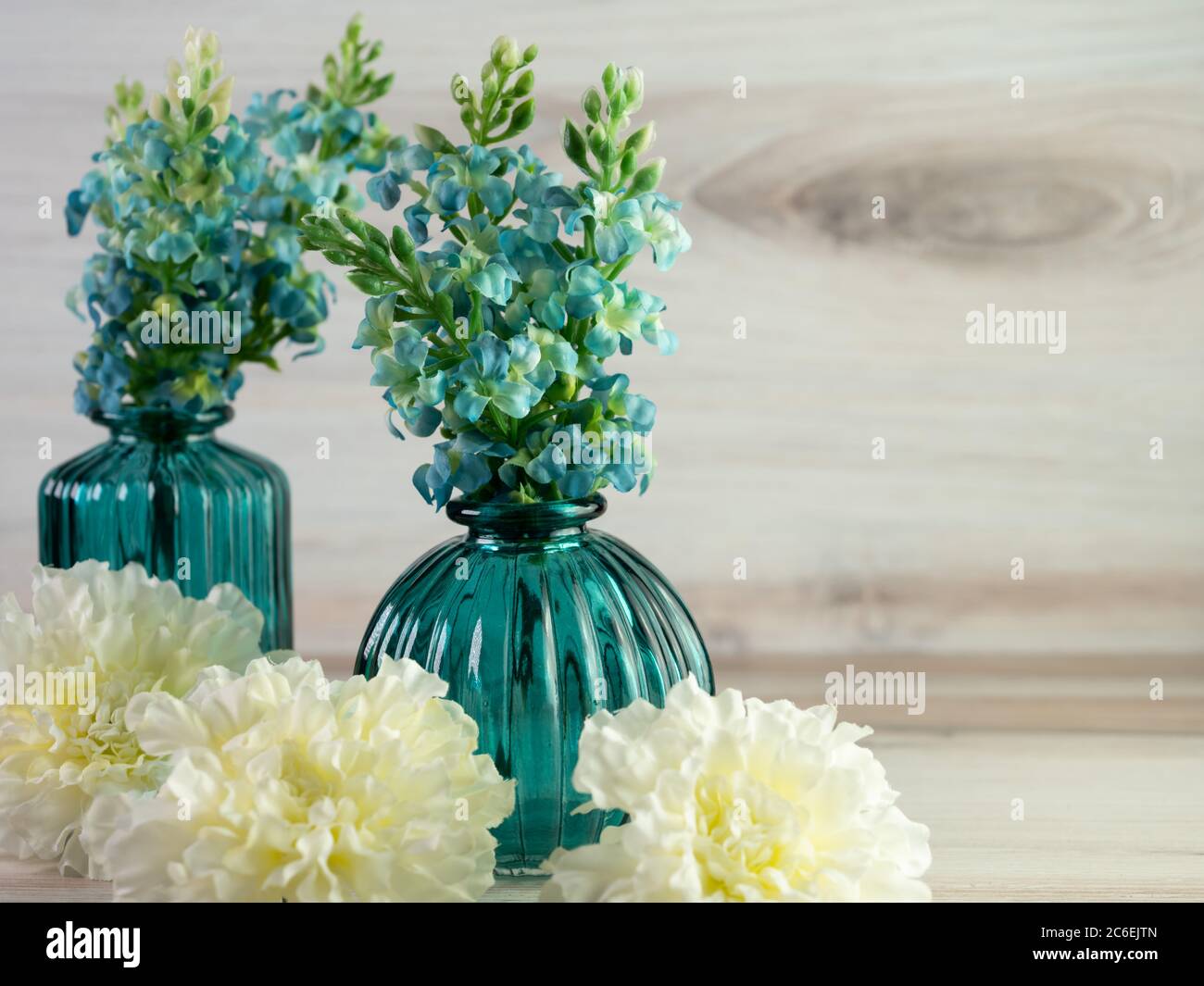 Dos jarrones de vidrio verde azulado de cerca con flores de hortensias  azules y claveles blancos en frente de ellos sobre un fondo de madera de  playa. Decoración de casa, simple y