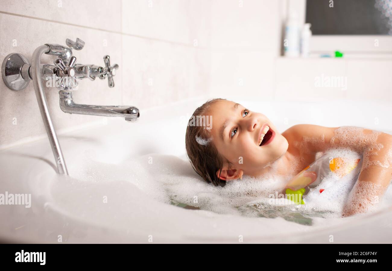 estanque Corte Gran cantidad de Una chica pequeña y divertida se baña en una bañera con una boya inflable y  con espuma en el agua. Concepto de higiene y entretenimiento para niños.  Advertis Fotografía de stock -