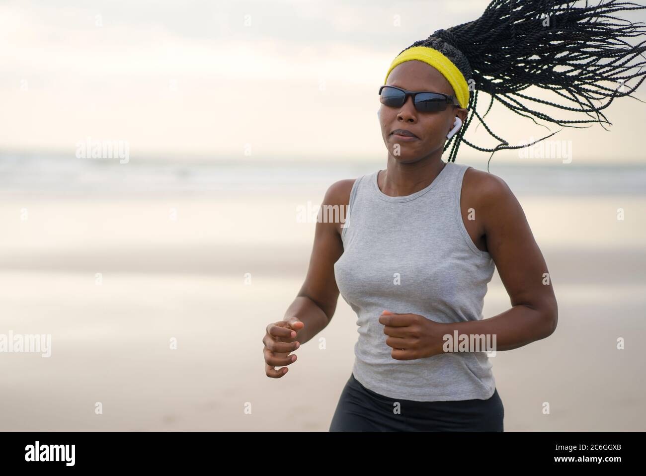 Mujer afroamericana corriendo en la playa - joven atractiva y deportiva chica negra entrenando al aire libre haciendo ejercicio de jogging en el mar en forma física Foto de stock