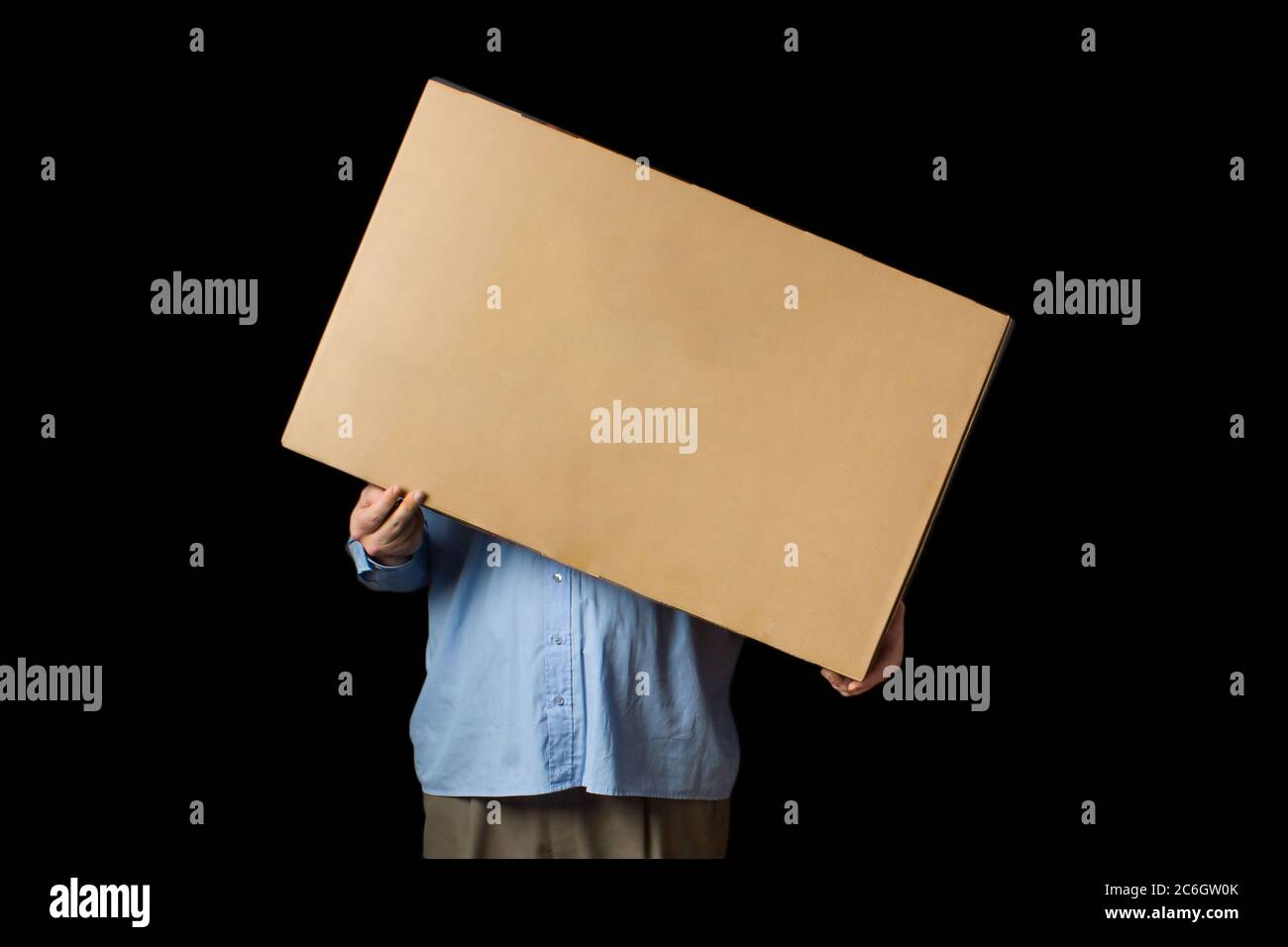 El hombre en la camisa azul sosteniendo en su mano una caja de cartón. Cubre su cara. Entrega de bienes de tiendas en línea. Foto de stock