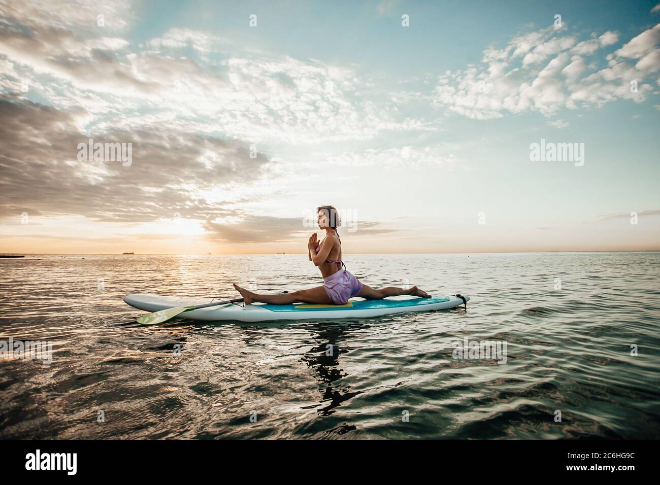 Mujer joven haciendo YOGA en una tabla de SUP en el lago al amanecer Foto de stock