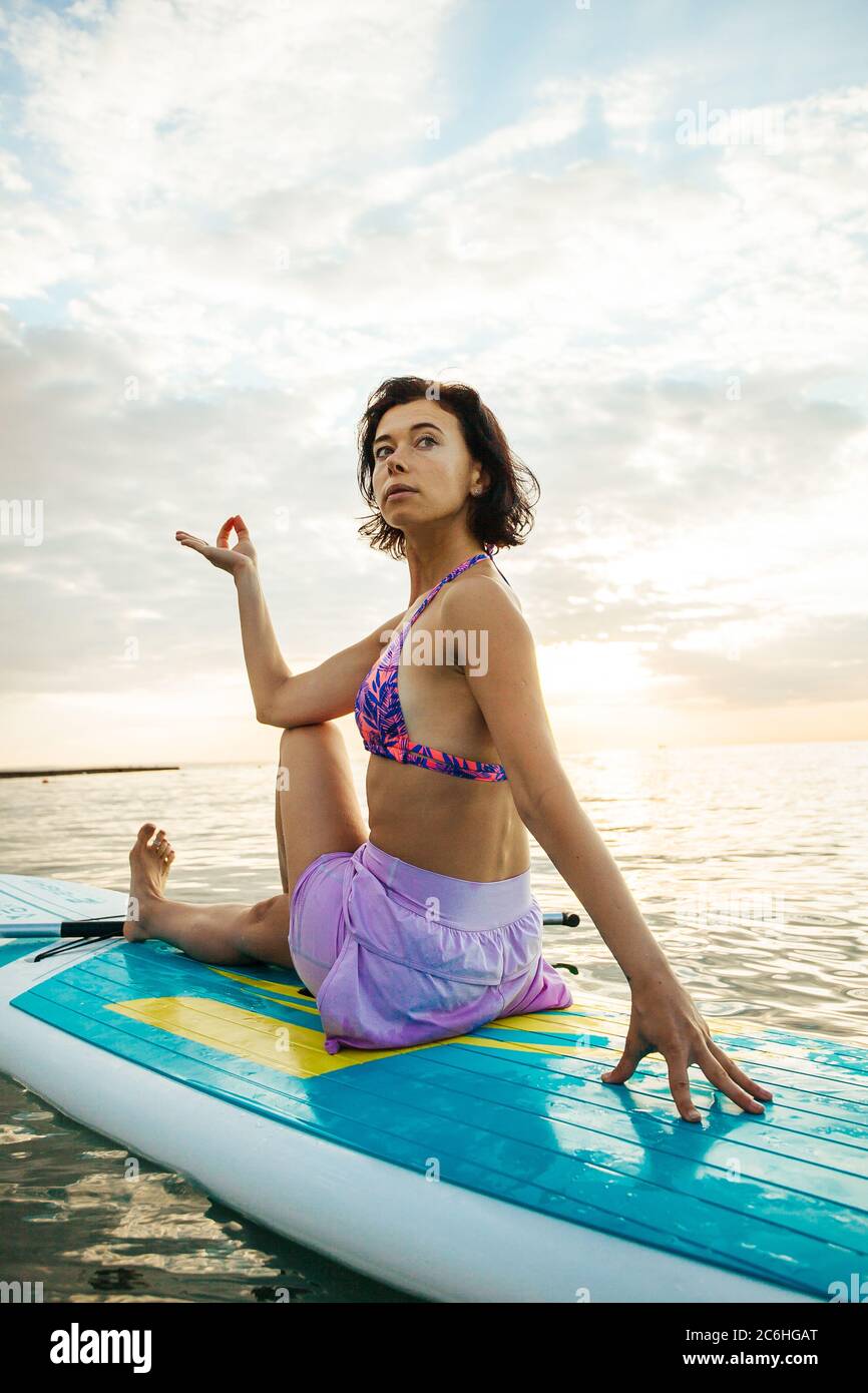 Mujer joven haciendo YOGA en una tabla de SUP en el lago al amanecer Foto de stock