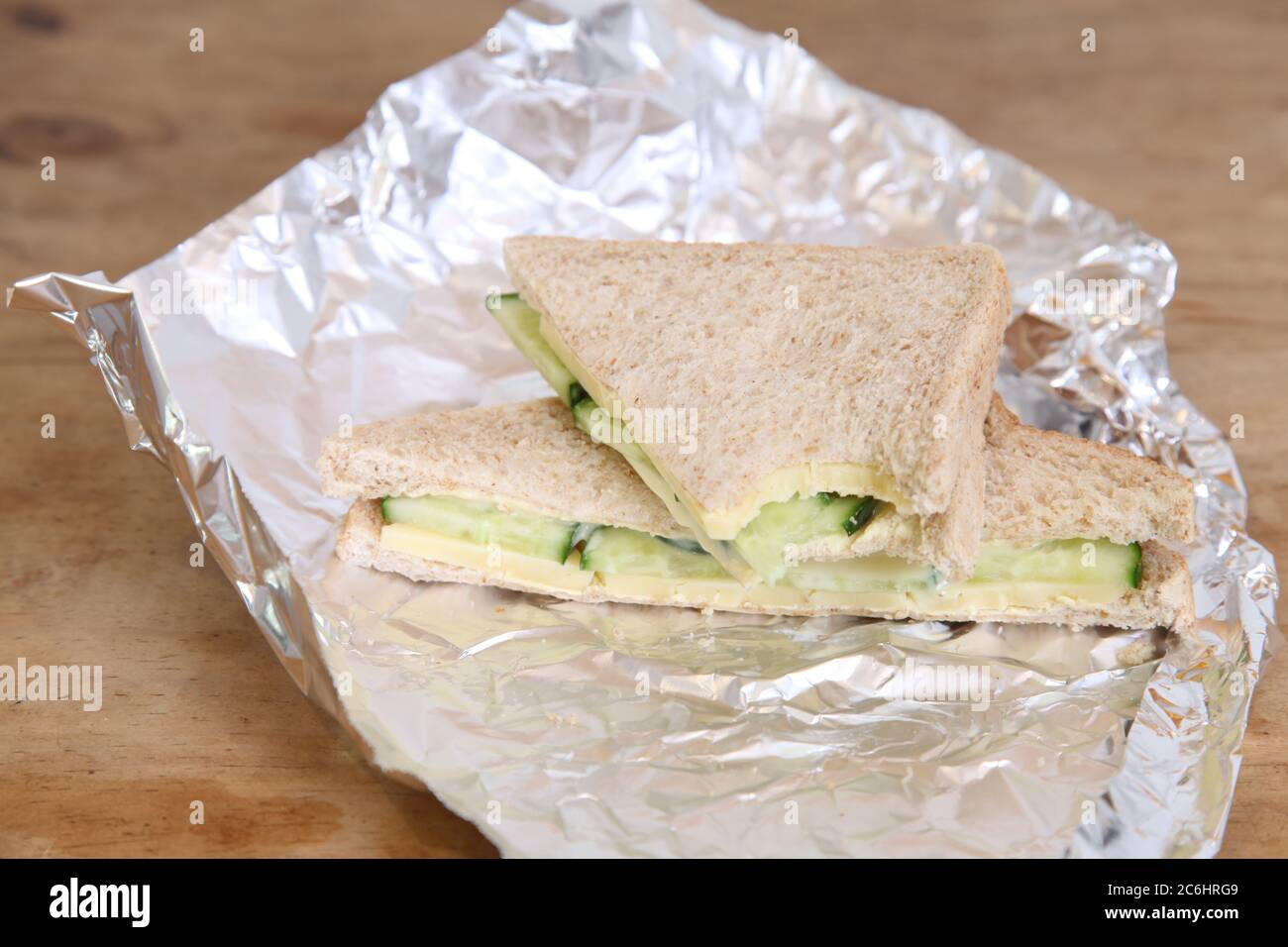 https://c8.alamy.com/compes/2c6hrg9/almuerzo-de-media-comida-de-sandwich-de-queso-y-pepino-en-papel-de-aluminio-sobre-mesa-de-madera-2c6hrg9.jpg