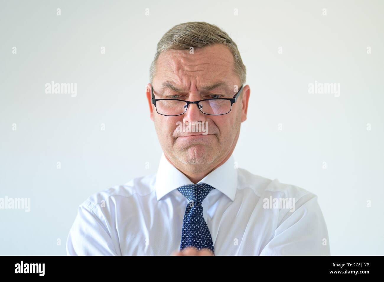 Hombre de negocios malhumorado con gafas mirando hacia abajo con una grimace en un retrato de cabeza y hombros en blanco Foto de stock