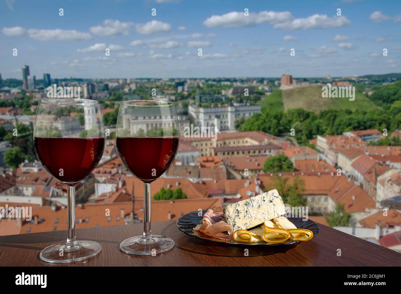 Dos copas de vino con surtido de charcutería a la vista de Vilnius, Lituania. Copa de vino tinto con diferentes aperitivos - plato con jamón, cortado en rodajas, azul Foto de stock