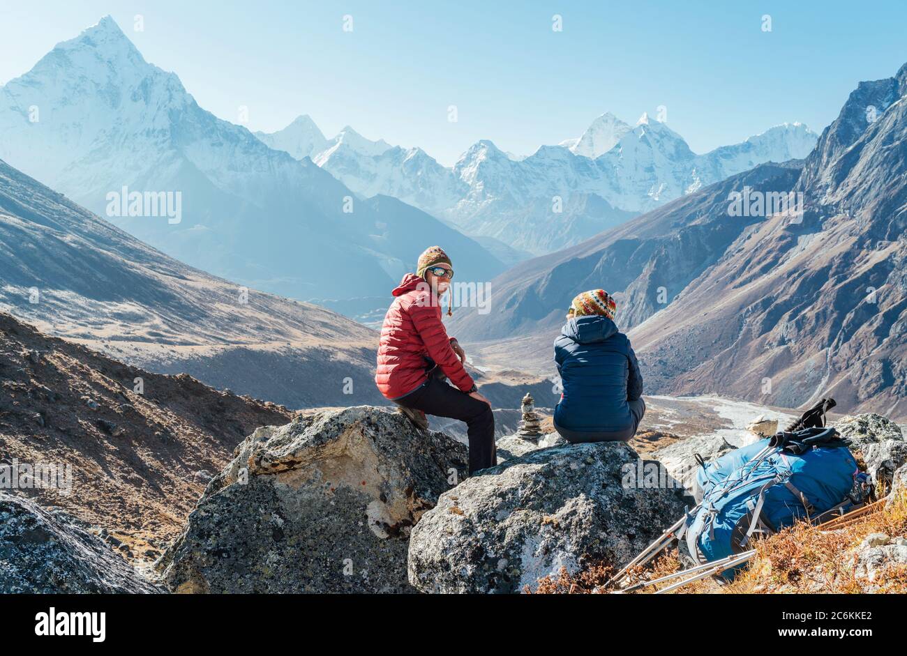 Pareja linda descansando en la ruta de senderismo Everest base Camp cerca de Dughla 4620m. Hombre sonriendo a woman.Backpackers izquierda mochilas y bastones de senderismo y.. Foto de stock