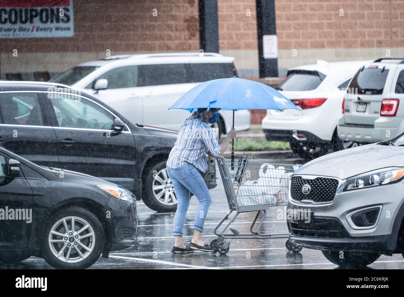 Mujeres mayores que empujan el supermercado en el estacionamiento bajo la lluvia. Foto de stock