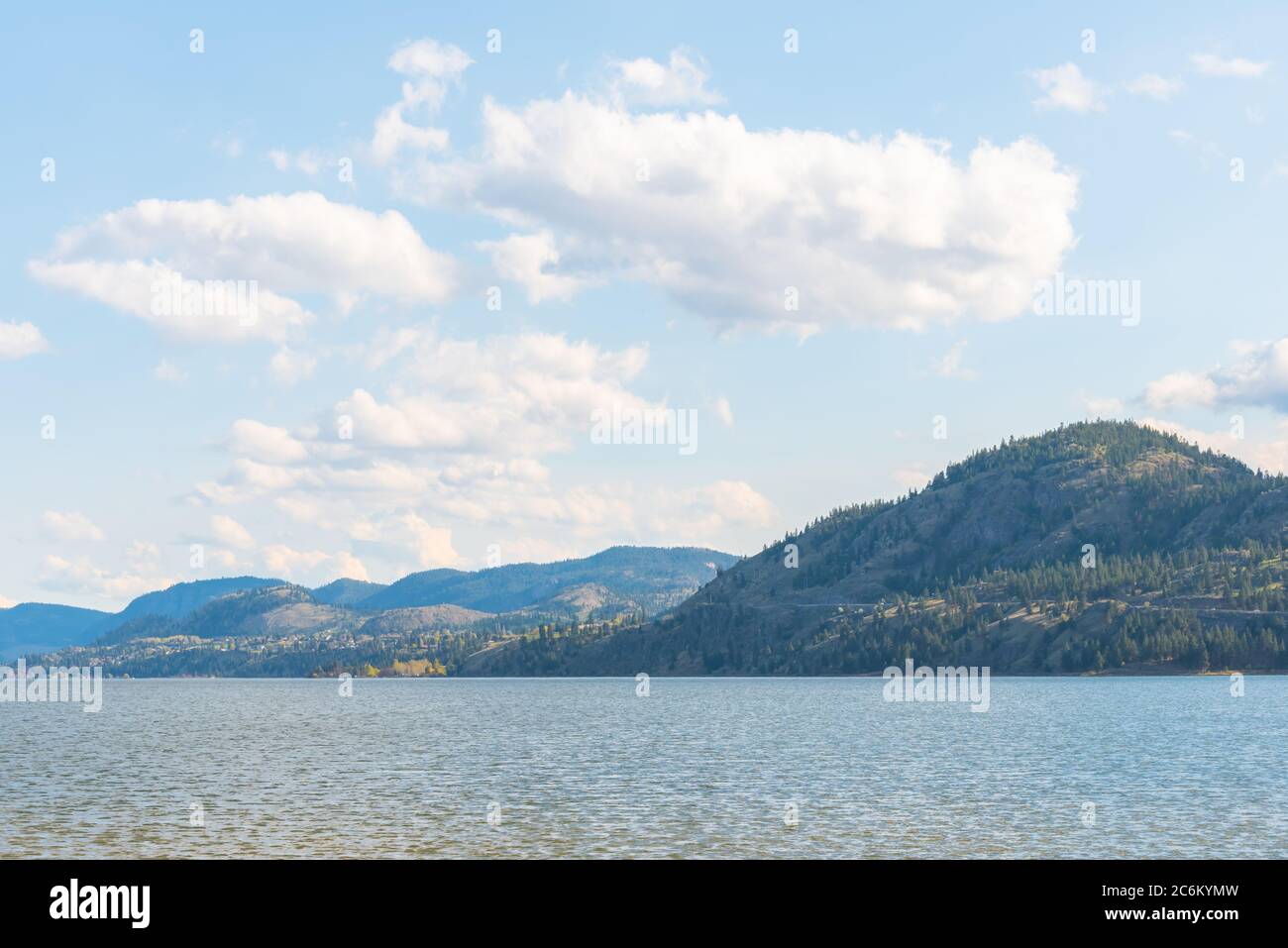 Vista de lago tranquilo, montañas boscosas, y cielo azul con nubes. Foto de stock
