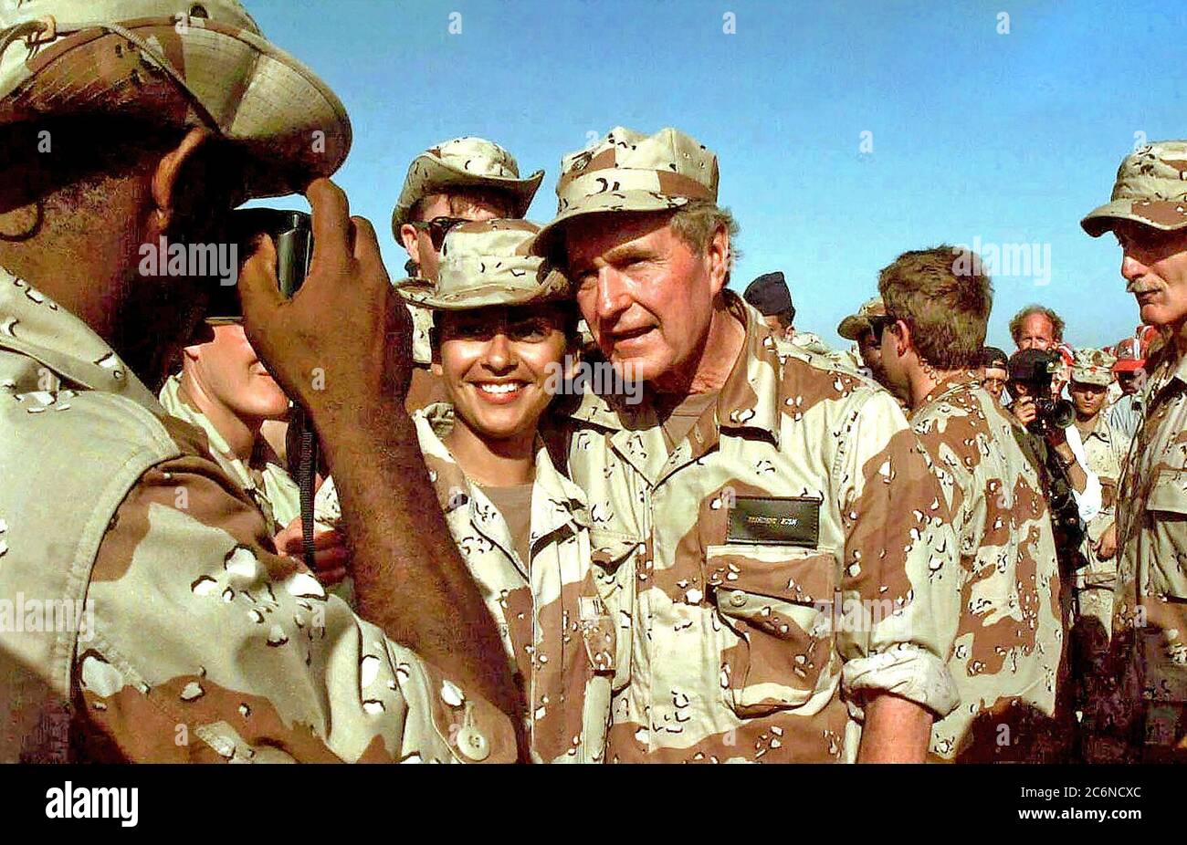 1993 - Medio de cerca del Presidente americano Bush teniendo tomé para posar para una foto con una mujer no identificada de los miembros de las fuerzas de los EE.UU. asignados a la misión en Somalia. Un gran número de otros miembros de la fuerza se han reunido en torno al Presidente. El Presidente visitó Somalia es mostrar gratitud a aquellos que participan en la misión de la operación Restaurar la esperanza. Foto de stock