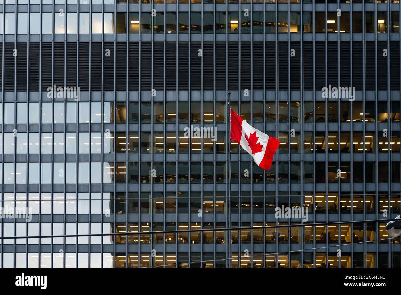 Bandera canadiense frente a un moderno edificio de oficinas al atardecer en el centro de Toronto, con espacios de oficina iluminados. Foto de stock