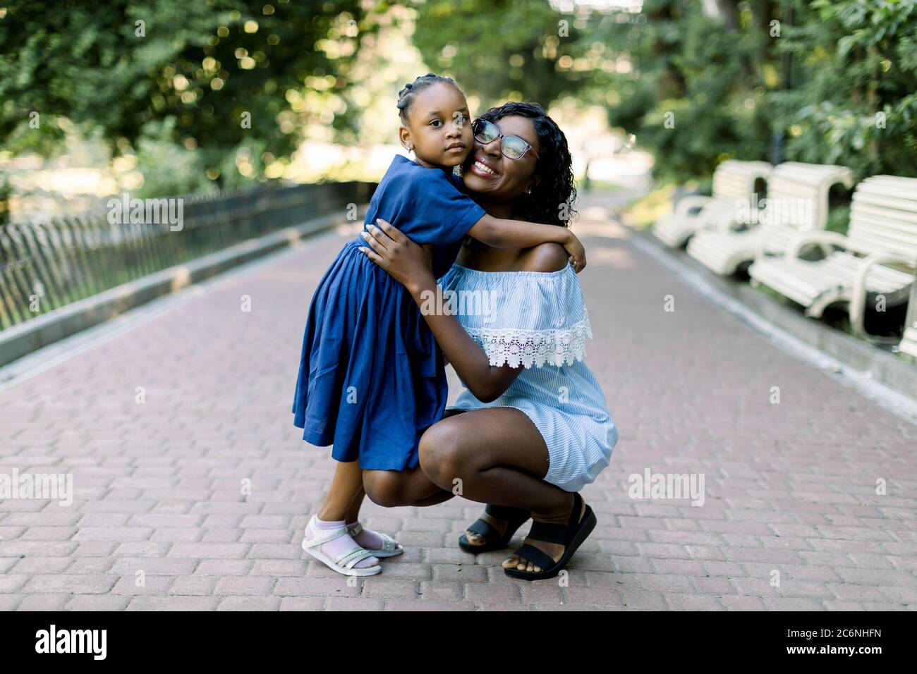 Retrato de una joven y sonriente madre africana feliz abrazando a su hija pequeña con ternura y amor en el parque. Madre y. Foto de stock