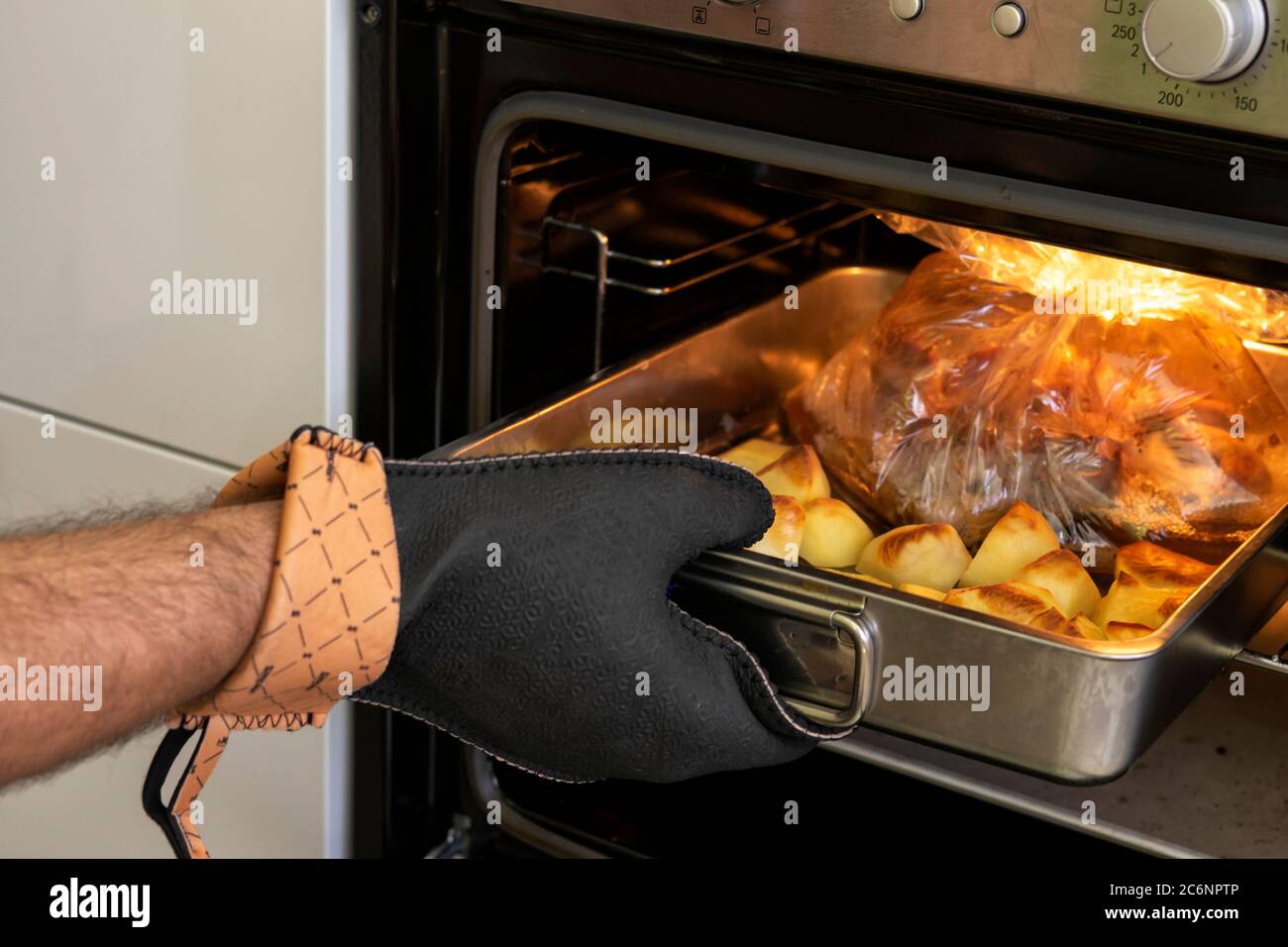 un hombre en un guante resistente saca comida horneada del horno Foto de stock