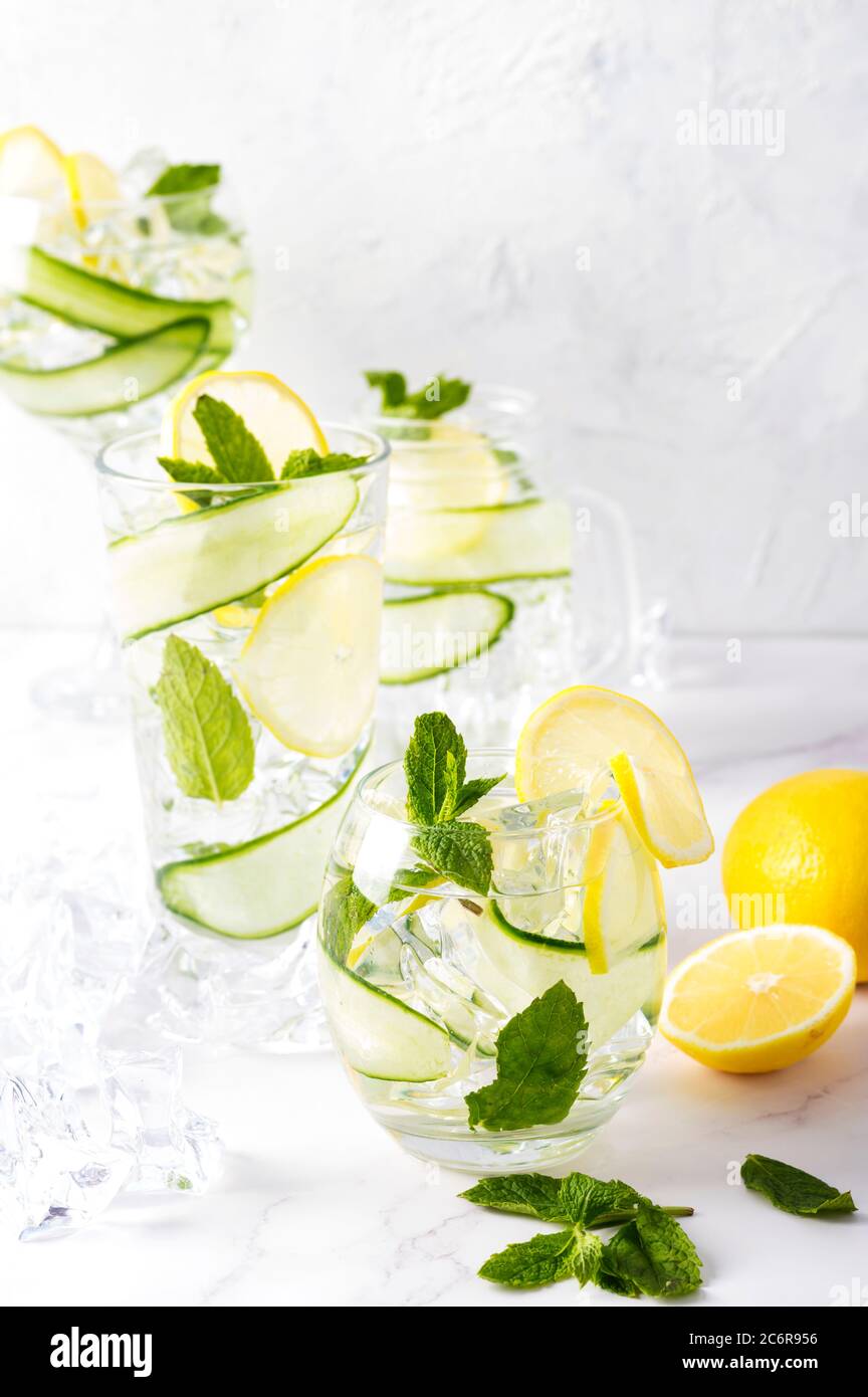 Bebida alcohólica (cóctel de tónico Ginebra) en una variedad de vasos con limón, pepino, hojas de menta y hielo sobre blanco. Bebida helada con limón. Foto de stock