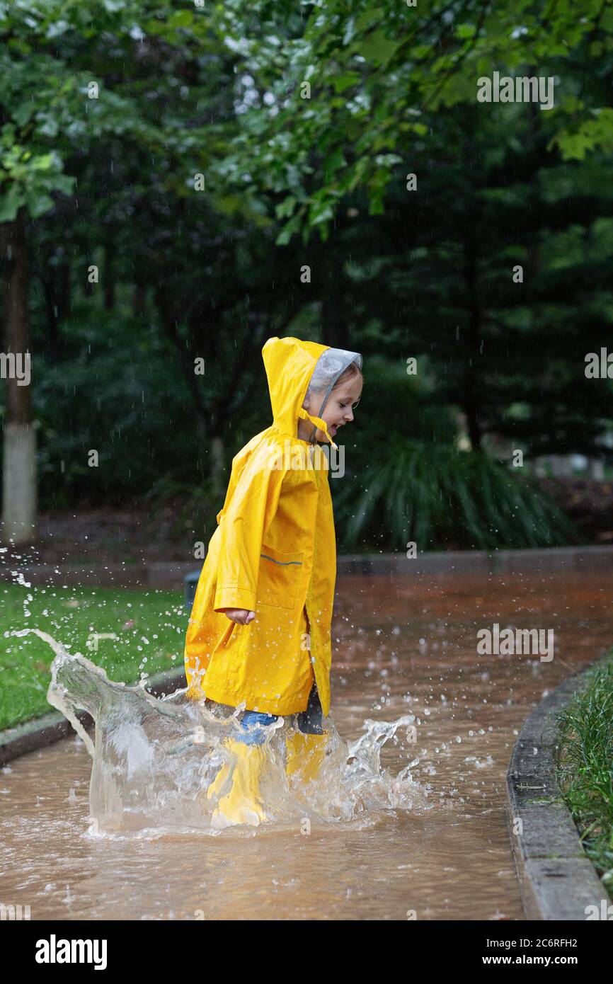 Linda niña en impermeable amarillo y botas de goma caminando al aire libre  durante la lluvia. Mal tiempo, tormenta tropical de verano, concepto de  moda de otoño Fotografía de stock - Alamy