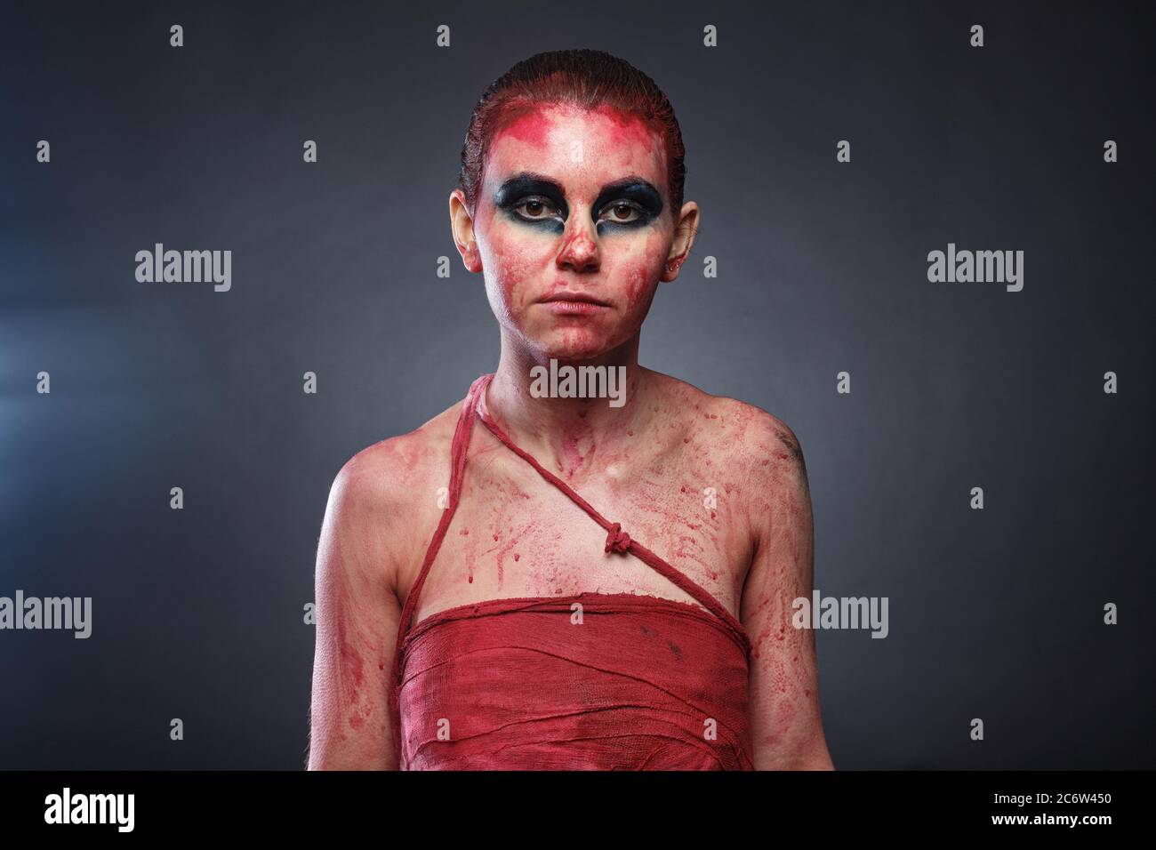 Foto mujer joven en sangre falsa sobre fondo gris Foto de stock
