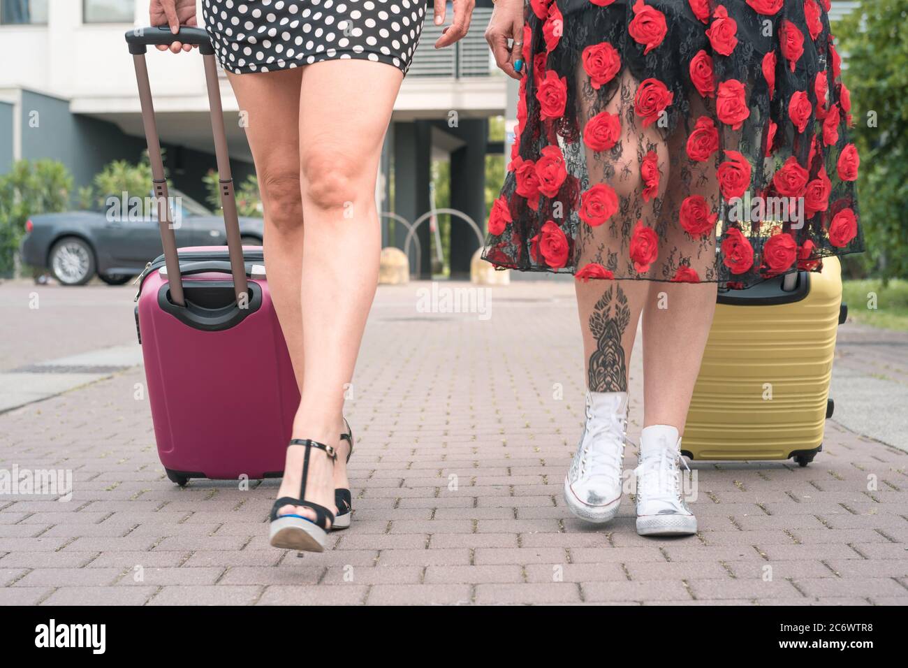 Foto recortada de abajo de dos mujeres turísticas elegantes caminando con  maletas en la calle floreada de la ciudad Fotografía de stock - Alamy