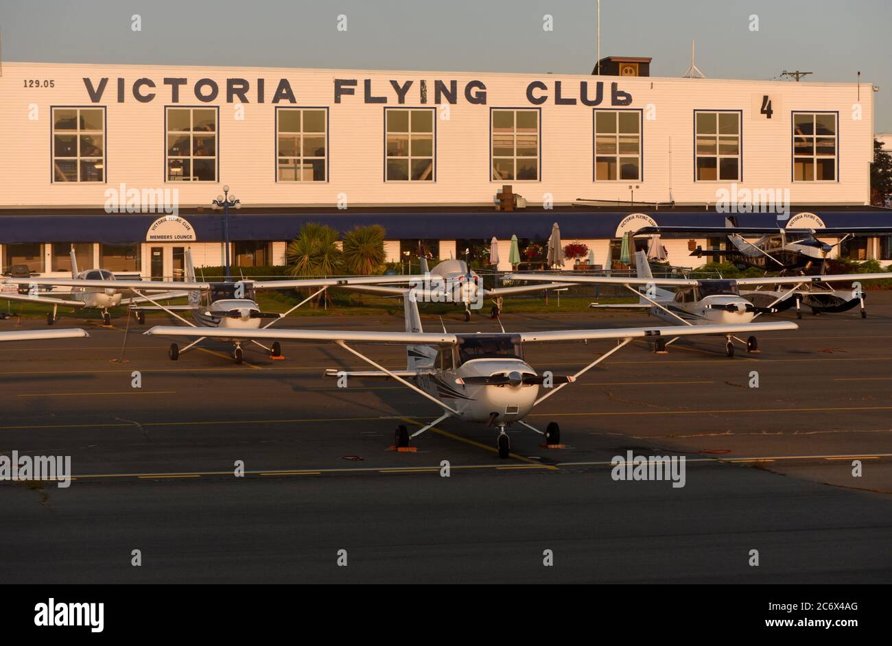 Los aviones pequeños se estacionan en el asfalto fuera del edificio Victoria Flying Club en el Aeropuerto Internacional de Victoria al atardecer en Sidney, Briti Foto de stock