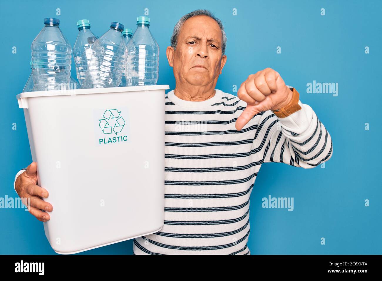 Hombre mayor reciclando la basura de la retención de la lata con botellas de  plástico para reciclar sobre fondo azul con cara enojada, signo negativo  que muestra desagradar con los pulgares Fotografía