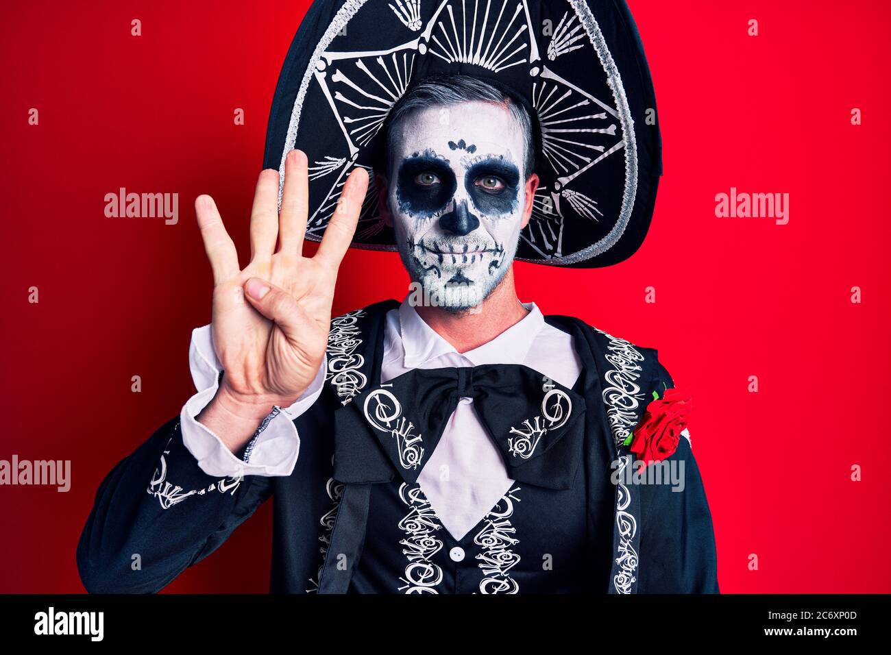 Joven que viste el día mexicano del traje muerto sobre rojo mostrando y señalando con los dedos número cuatro mientras sonríe confidente y feliz. Foto de stock