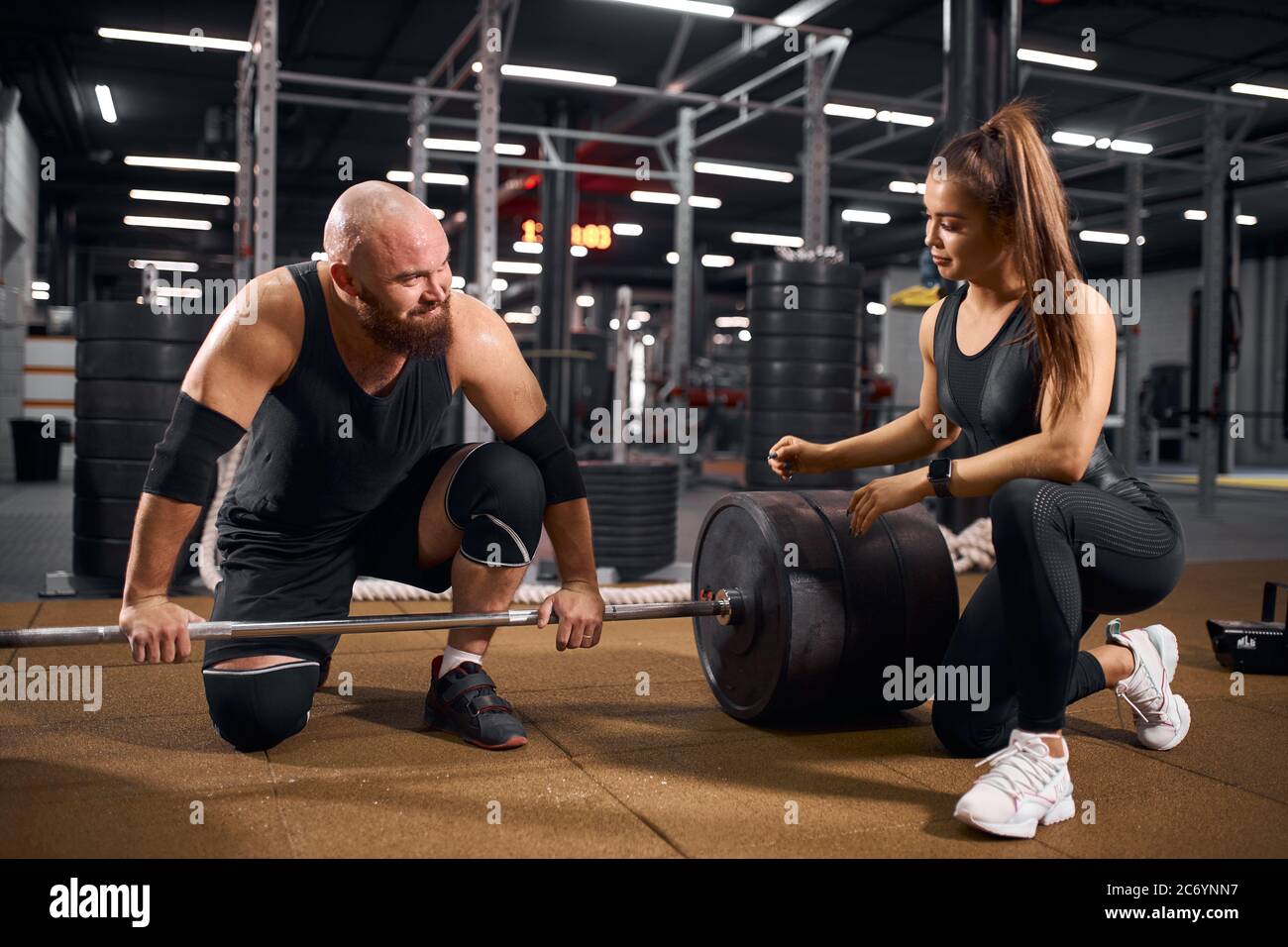 Retrato de una joven pareja deportiva pasando tiempo en el moderno  gimnasio, sentado en el suelo, apoyado en una campana negra, mirando,  hablando apasionadamente Fotografía de stock - Alamy
