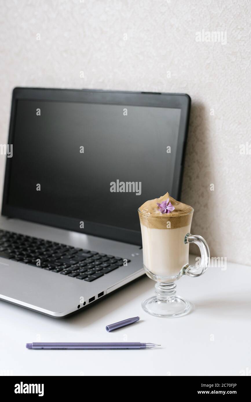 Café Dalgona en una taza transparente, Bloc de notas, pluma y ordenador en la mesa. Vista superior. Café en el lugar de trabajo de un blogger o freelancer Foto de stock