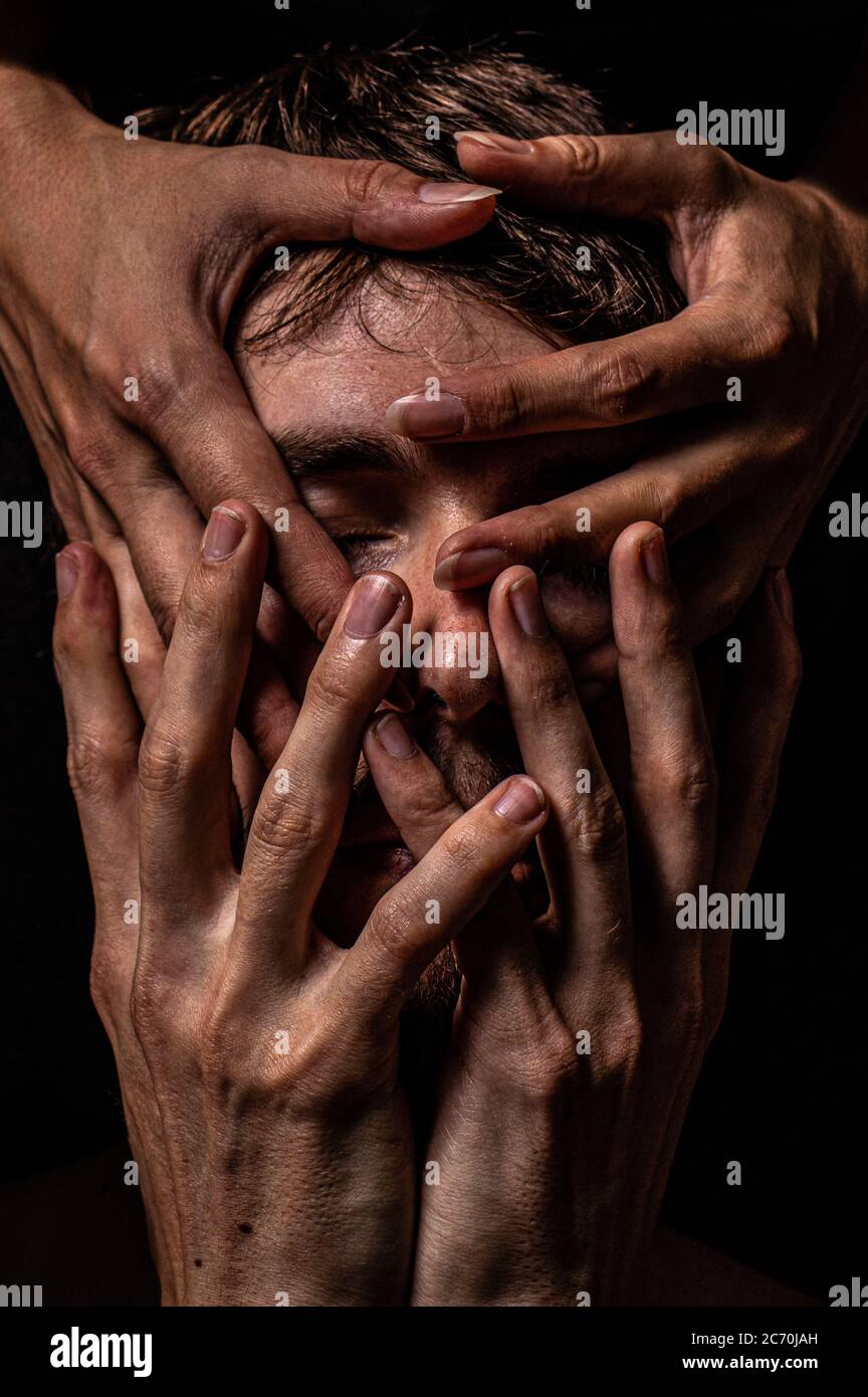 Cuatro manos cubren la cara de un hombre casi por completo. Foto de stock
