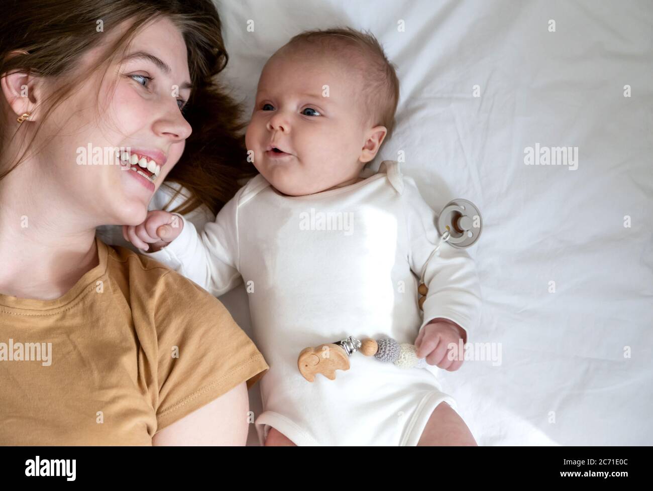 Feliz risa mamá y la hija se encuentran en sus espaldas. Feliz y sonriente madre y bebé tumbado en la cama en casa, vista superior. Foto de stock
